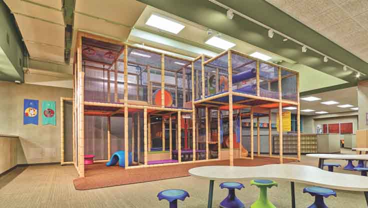 A spacious children’s play area with a double-decker climbing structure, tables and colorful stools