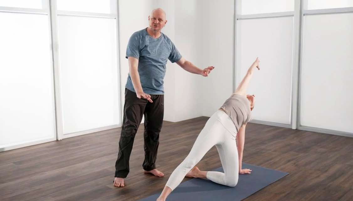Male yoga teacher instructing woman as she does a modified back bend