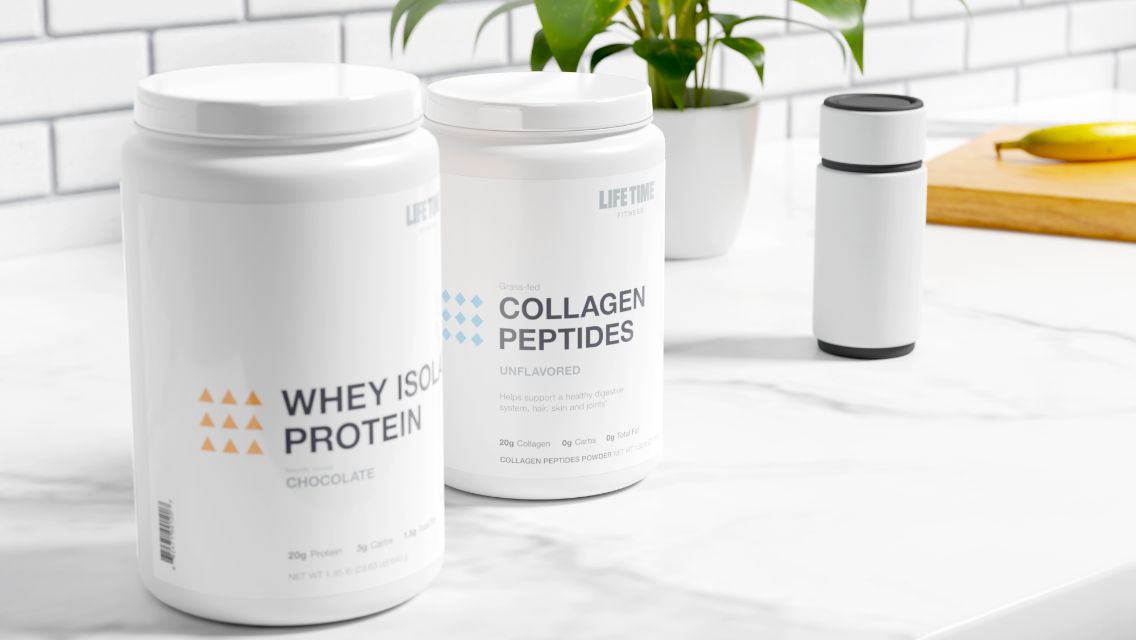 A container of Life Time’s Whey Isolate Protein powder and a container of Life Time’s Collagen Peptides sit on top of an elegant, white marble countertop in front of a white, subway tiled back splash. 