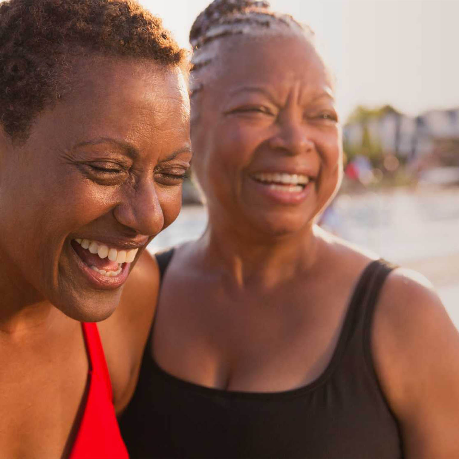 Two women wearing swim suits near the pool laughing together. 