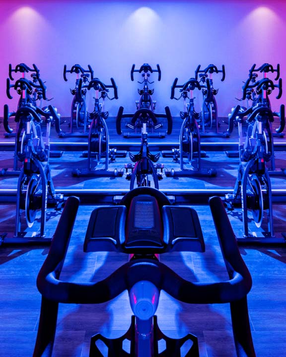 Rows of indoor bikes in a cycle studio at Life Time with colorful lights