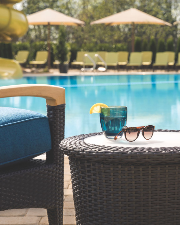 Drinks and sunglasses on a table next to a beautiful outdoor pool