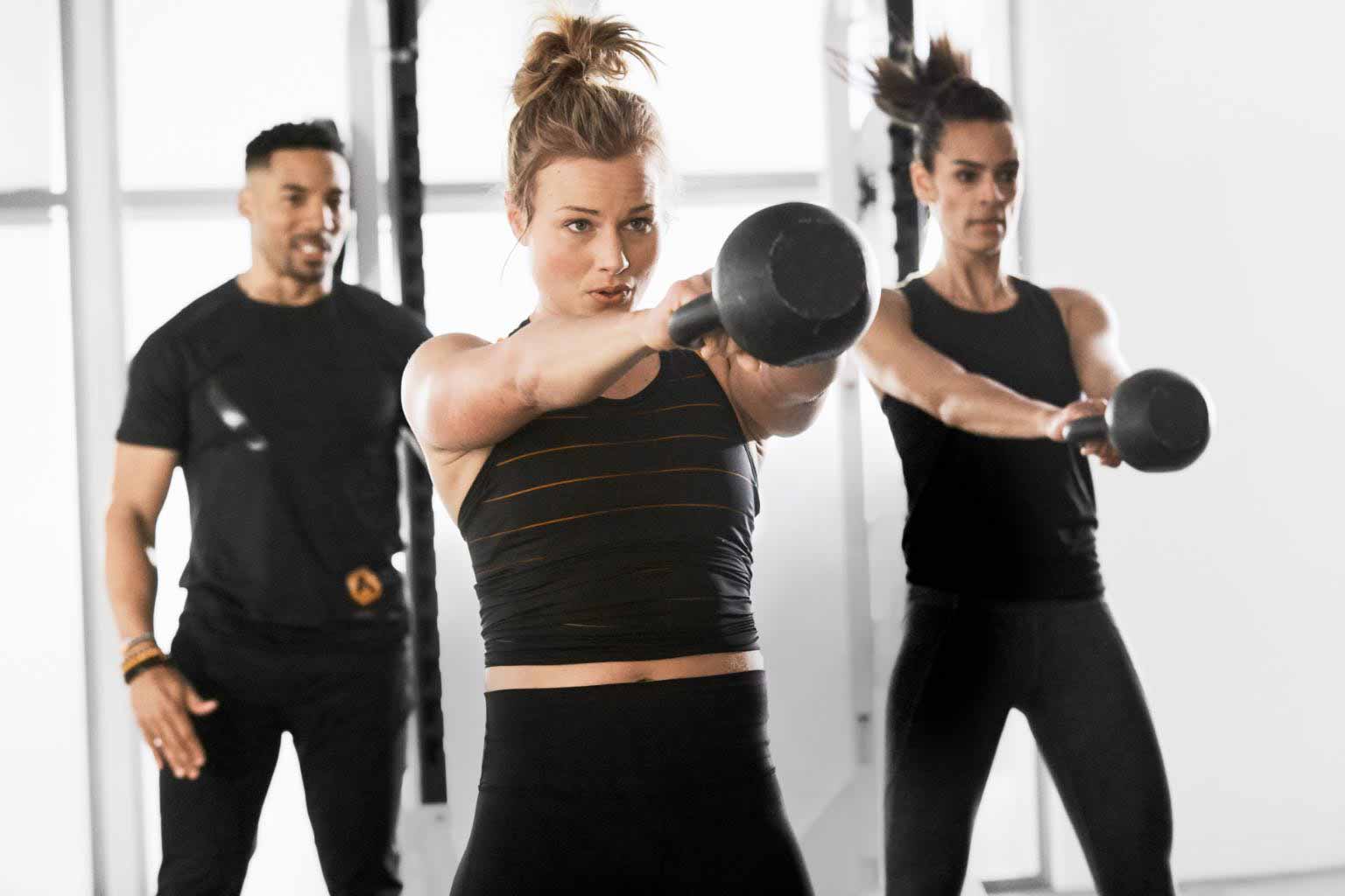 An alpha coach coaches 2 women doing a kettlebell exercise