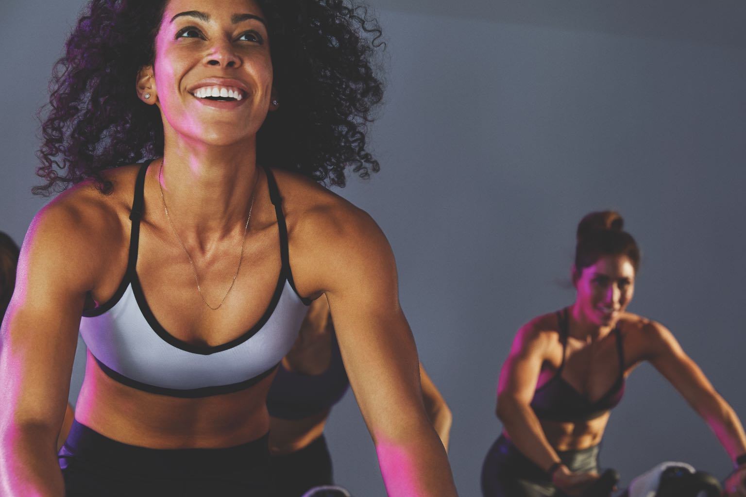 Closeup of woman in a cycle class, with other class participants behind her. 