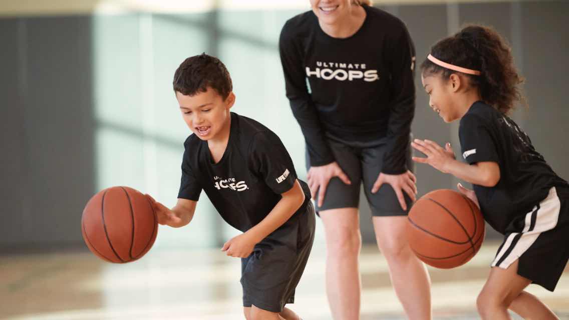 Coach watching two kids dribble basketball