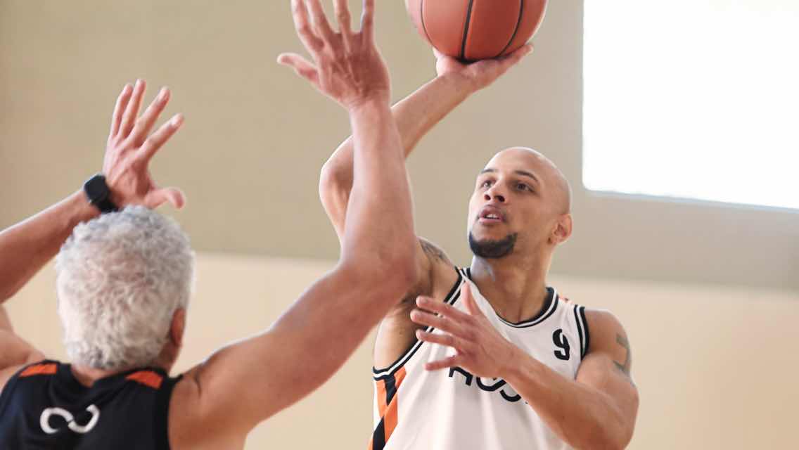 Man shooting basketball with another man guarding him. 