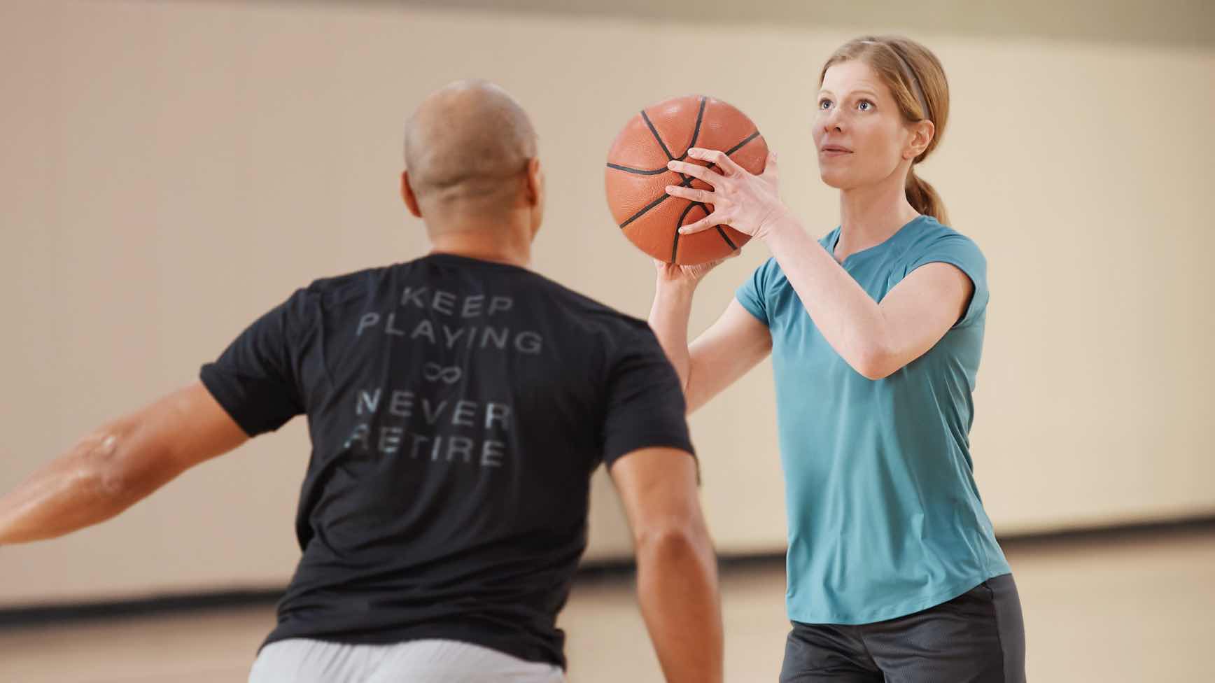 Woman shooting basketball with man guarding her