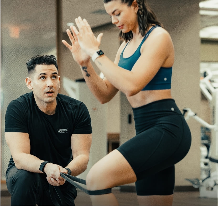 A male trainer conducting a movement screen with his client. He observes the woman as she lunges, assessing whether there are any muscular asymmetries that need to be addressed.