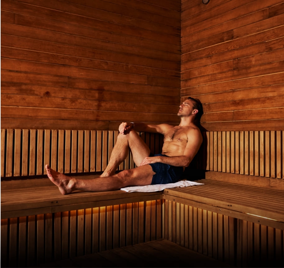 A man relaxing in the sauna. He sits in the corner of the cedarwood sauna with his legs up on the bench and his eyes closed, enjoying the stillness.