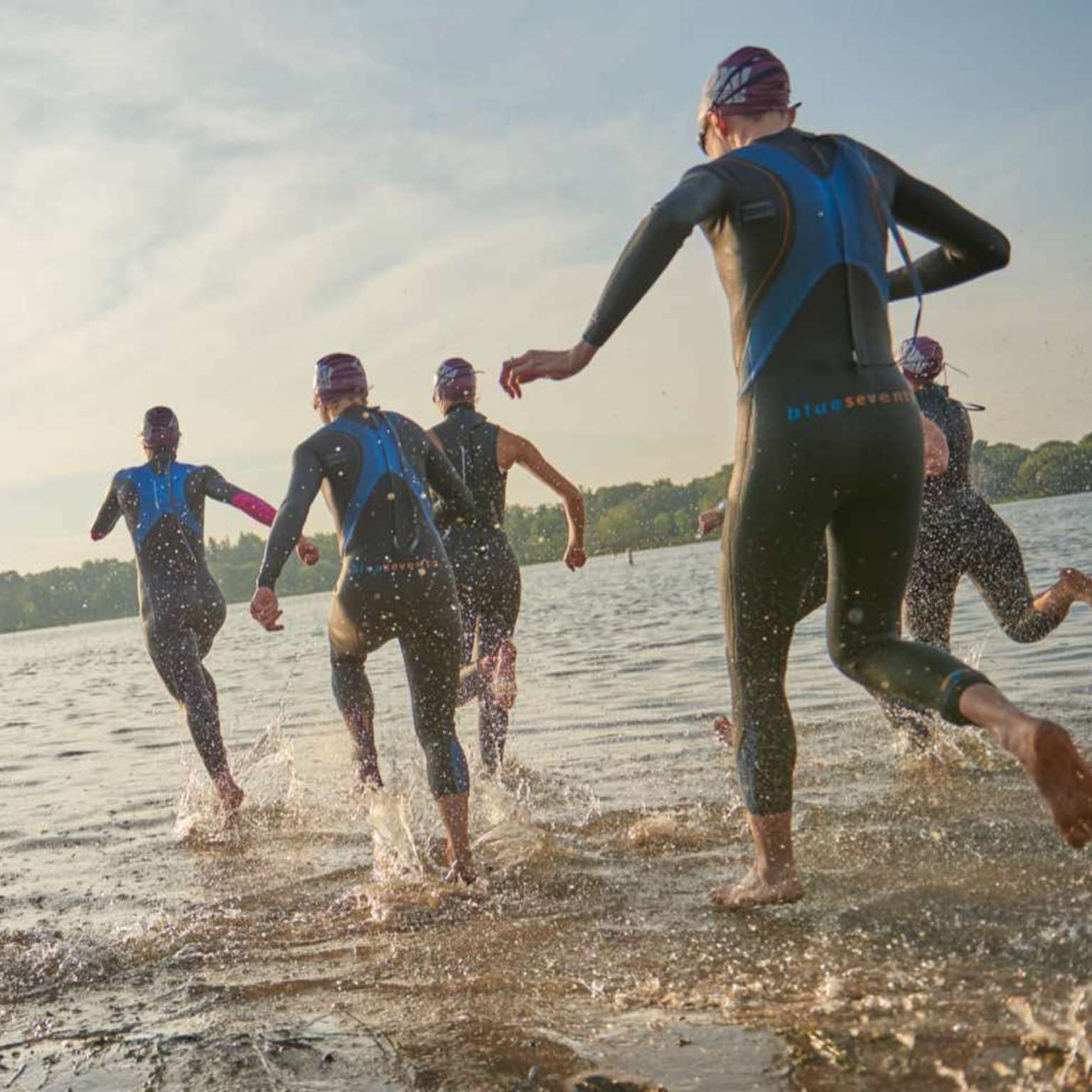 A group of people in wetsuits running into a lake during a triathlon event