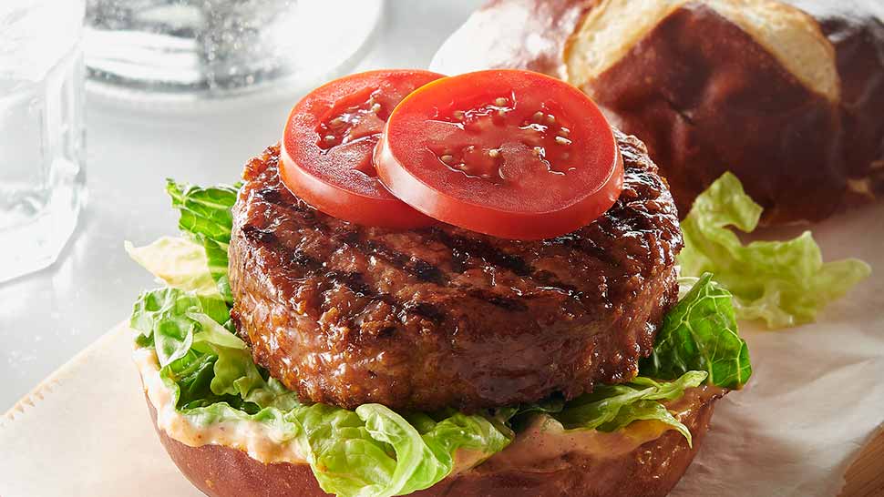 Juicy grass-fed burger on pretzel bun with lettuce and fresh tomato