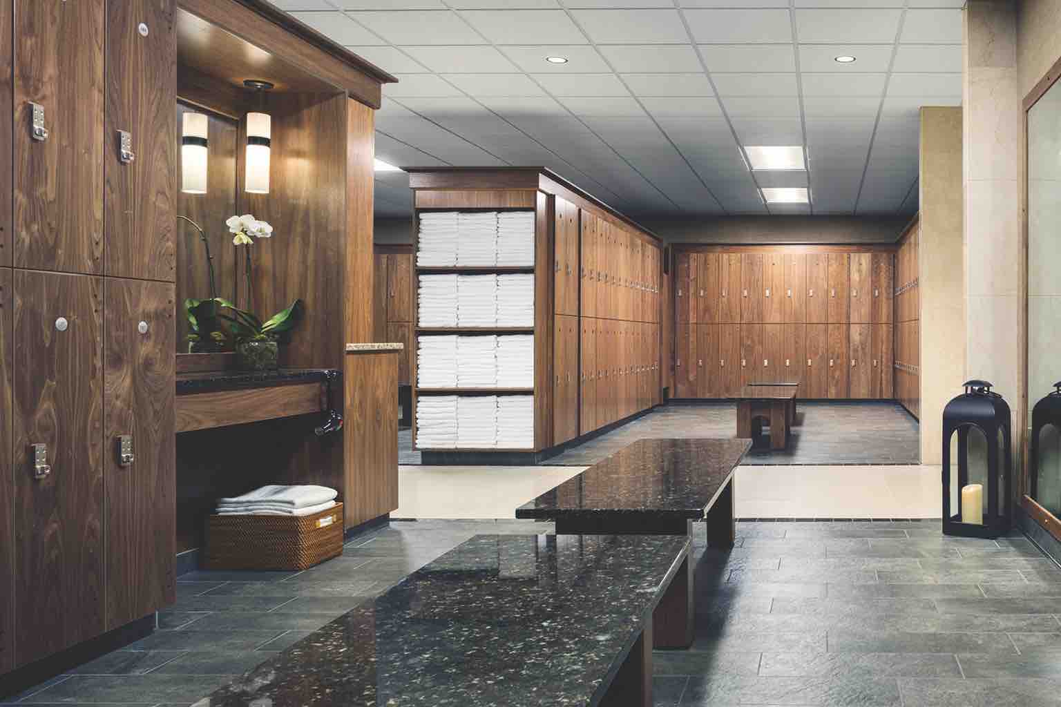 A luxurious locker room with rows of wooden lockers, a vanity area, benches and open shelving with stacks of white towels