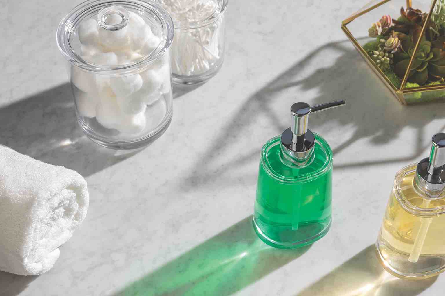 White and gray marbled counter top with two glass containers of cotton balls and cotton swabs, two hand soap pump dispensers and a crisp, rolled up towel