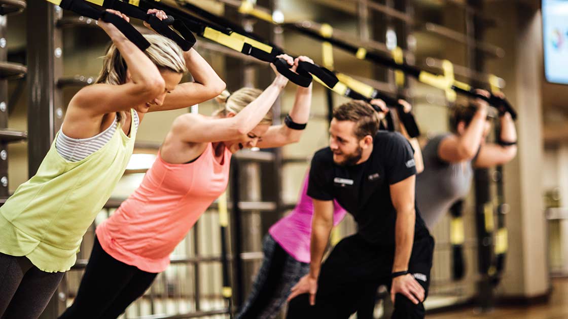 A Personal Trainer cheers on four clients as they work out in an Alpha Training area