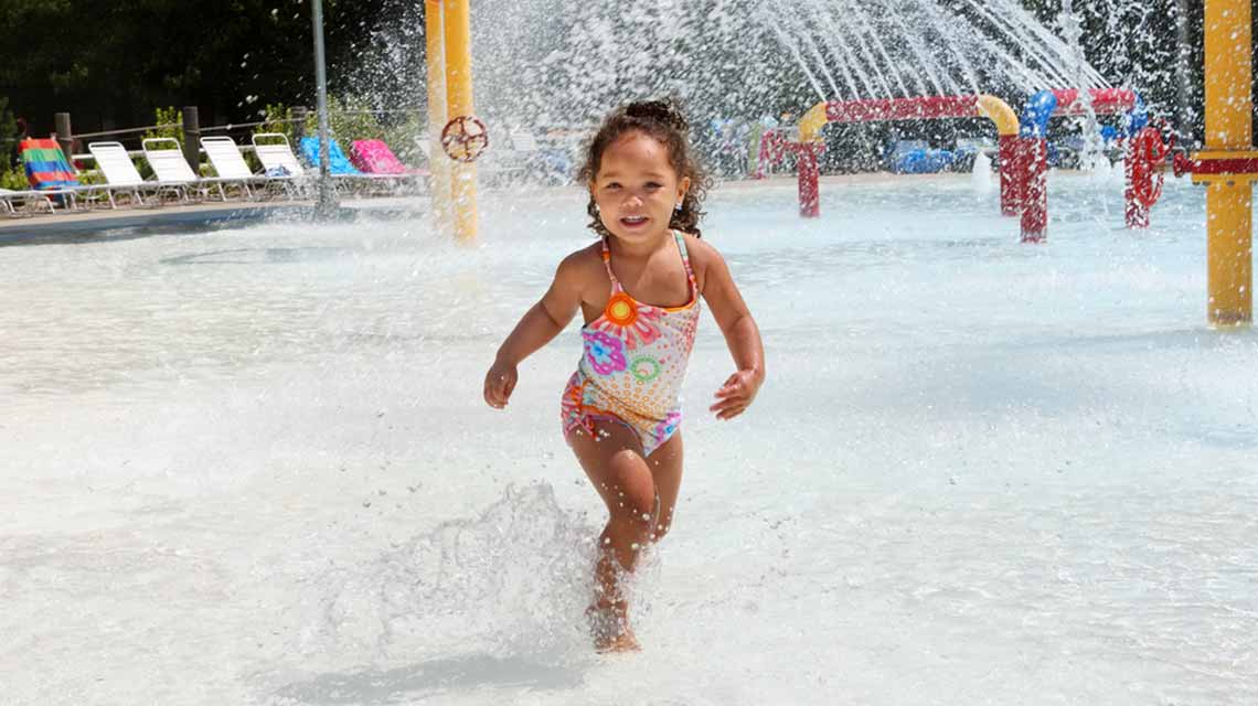 A little girl plays beneath the fountains in the outdoor pool splash pad