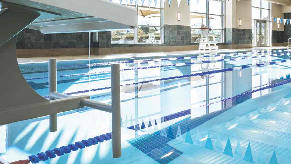 A brightly lit indoor lap pool with blue and white banners strung overhead 