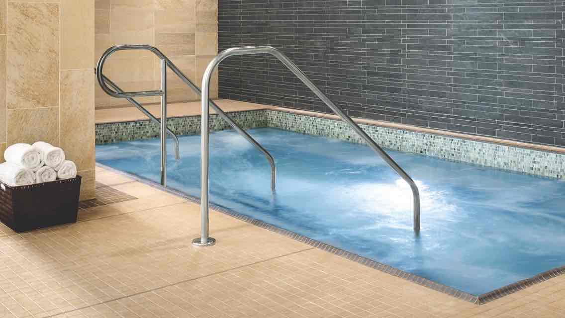 A basket of white towels sits by a spacious indoor whirlpool filled with crystal-clear water 