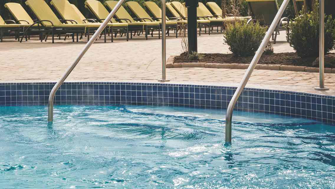 A row of outdoor lounge chairs sit beside an outdoor whirlpool filled with crystal-clear water