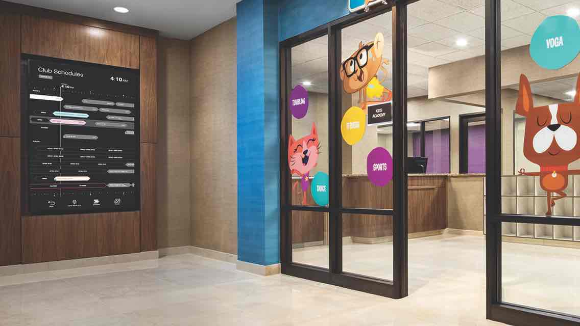 Sliding glass doors decorated with colorful stickers open to the front desk of the Kids Academy and a row of lockers and cubbies  