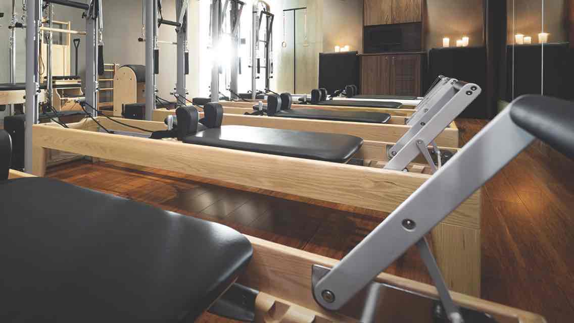 A candle-lit Pilates studio with glossy wood floors and a row of Pilates reformers