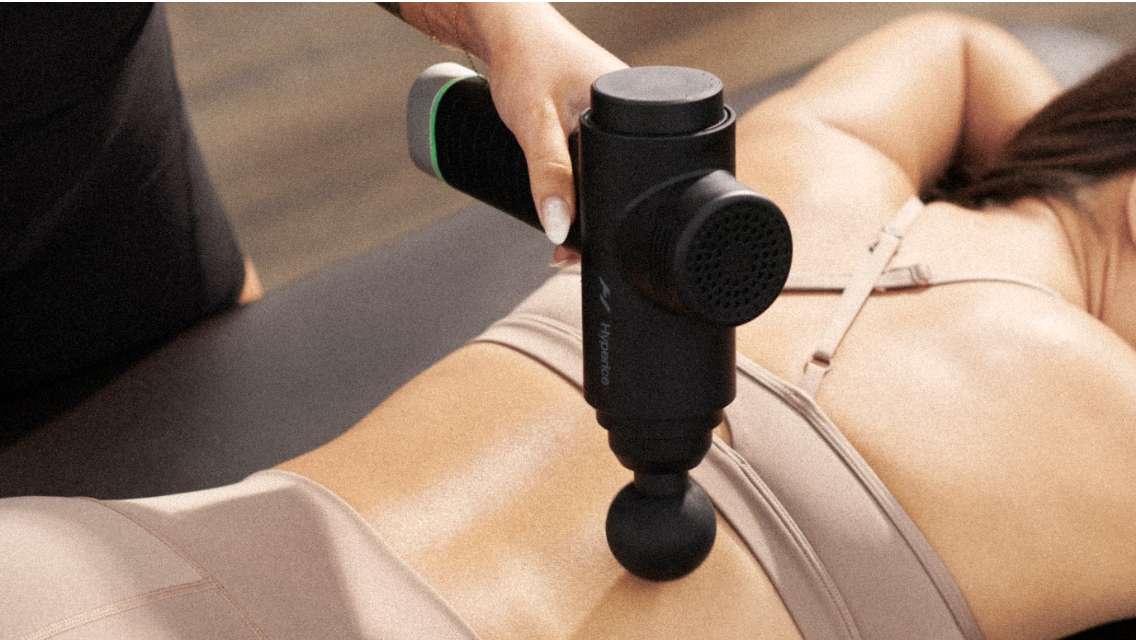 a trainer using a massage gun on a member