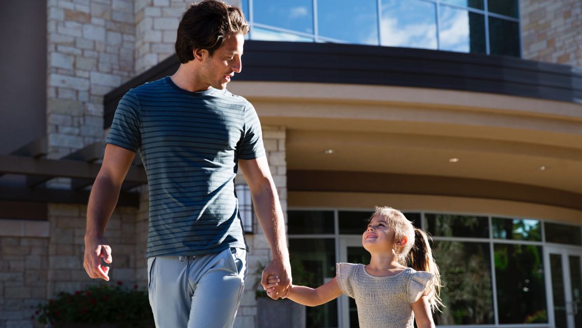 A father and daughter hold hands and smile at each other 