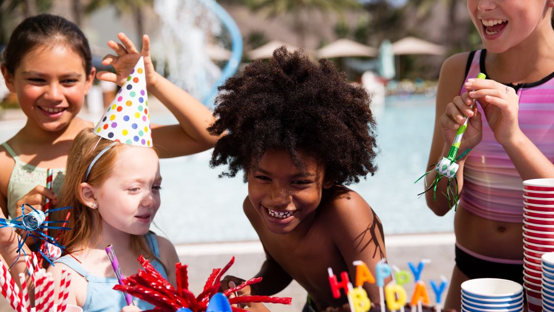 A group of kids gathered around a table with birthday hats and decorations