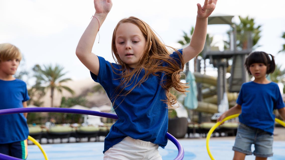 Three kids wearing blue shirts hula hooping at an outdoor playground