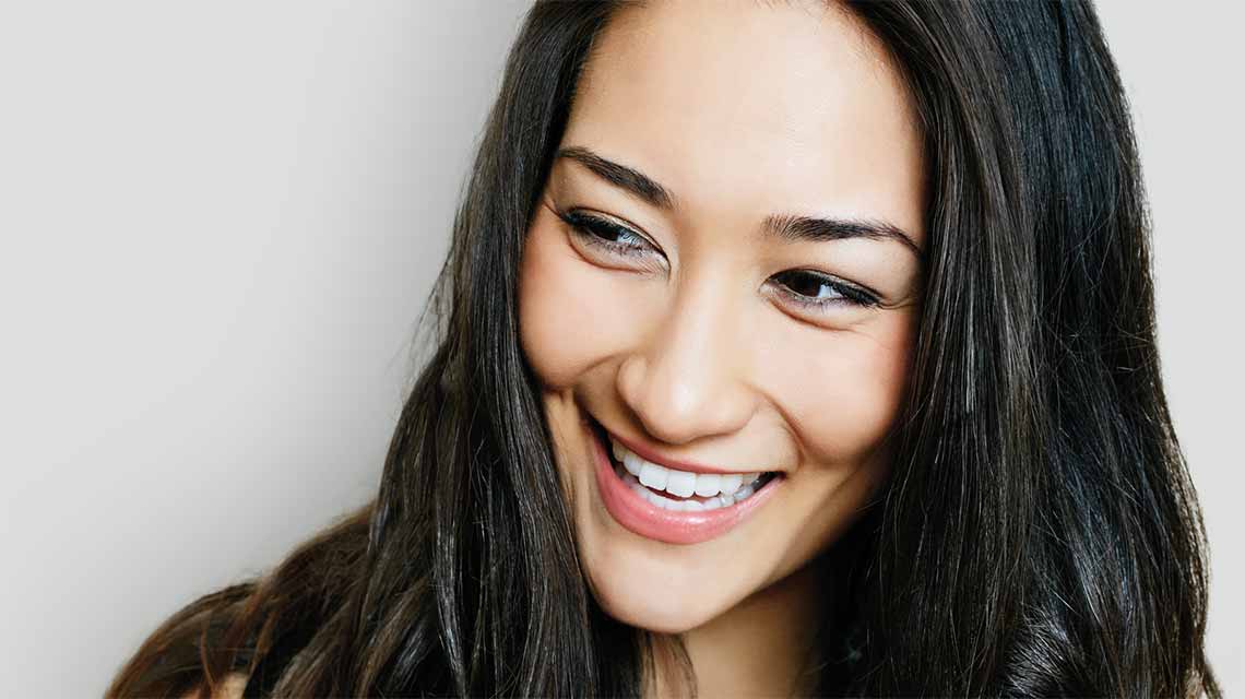 A woman with long, straight hair smiling and looking off to the side