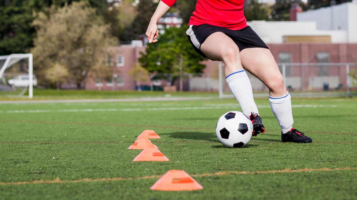 a soccer player kicking a ball around cones on a soccer field