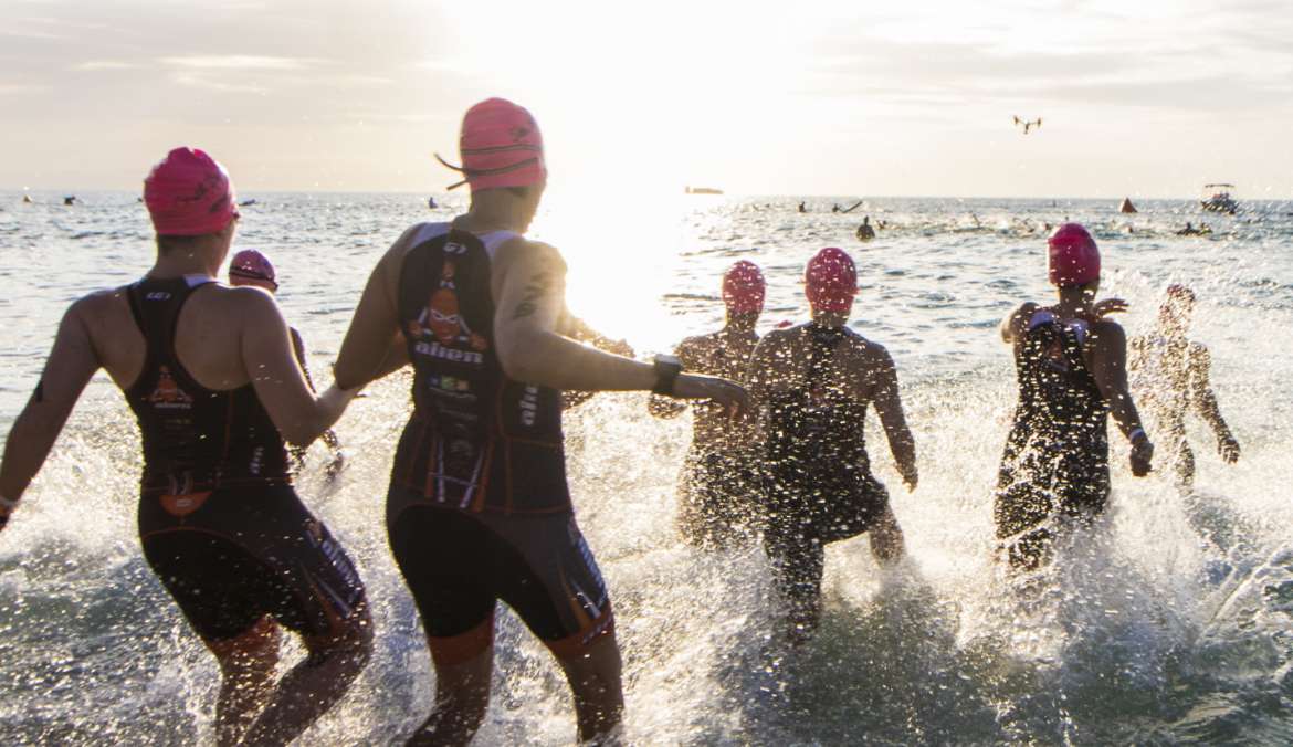 Triathlete swimmers run into the water to start their race.