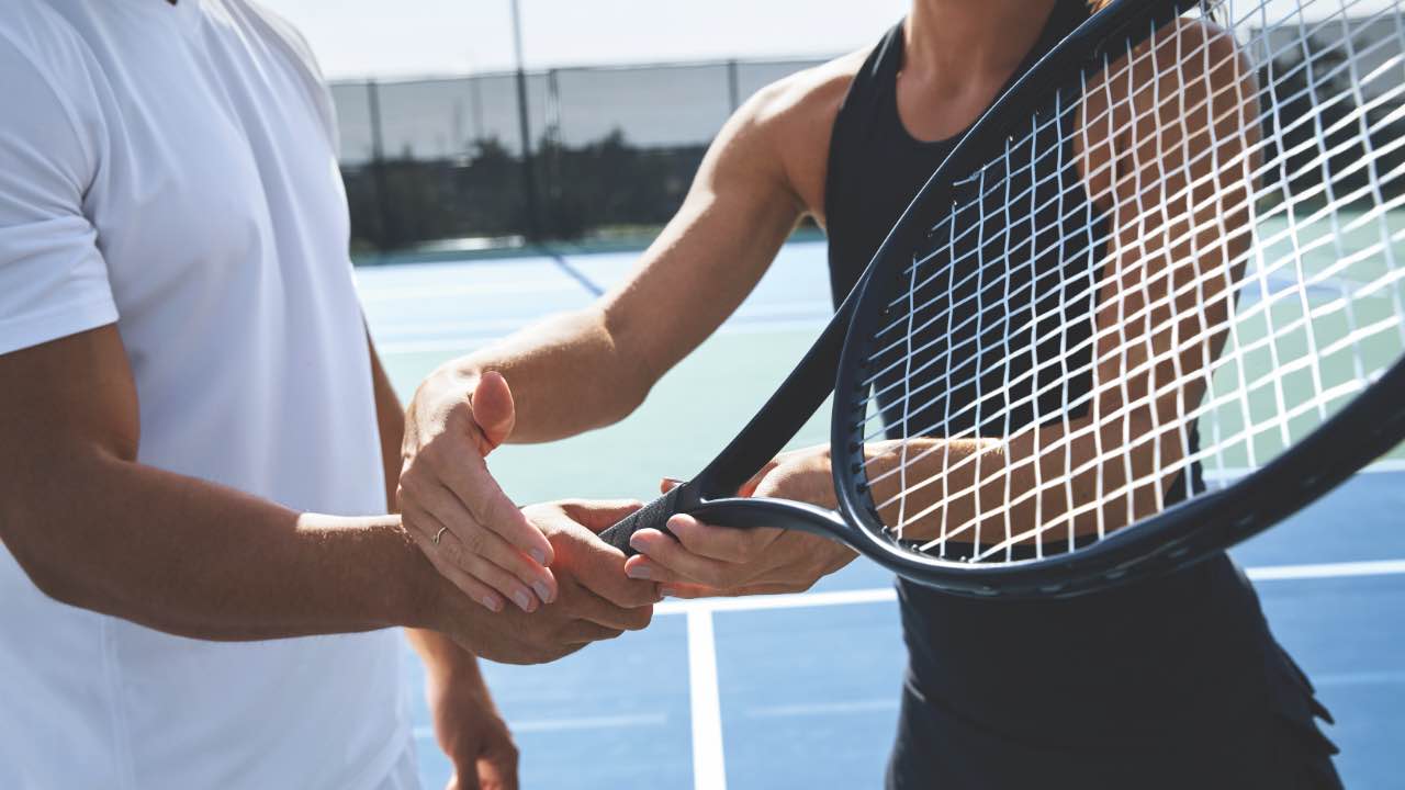 Closeup of woman showing a man how to hold a racquet. 