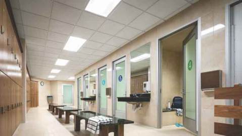 A spacious locker room area with lockers, benches, mirrors and numbered doors leading to private family changing rooms