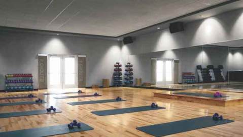 Grey yoga mats, each equipped with a pair of dumbbells, lined up on the gleaming wood floor of a mirrored studio 