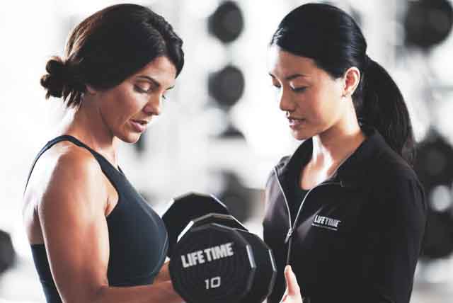 Two women dressed in workout clothes talking on the fitness floor of a gym  