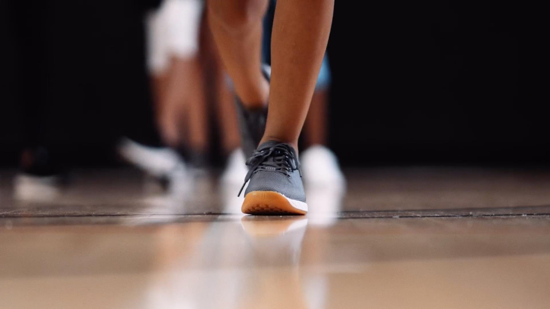 focus on a young athletes feet and shoes on a gym floor with other children's feet in the background