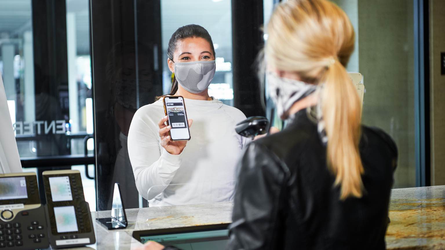 a life time employee wearing a mask scans a members phone at the front desk