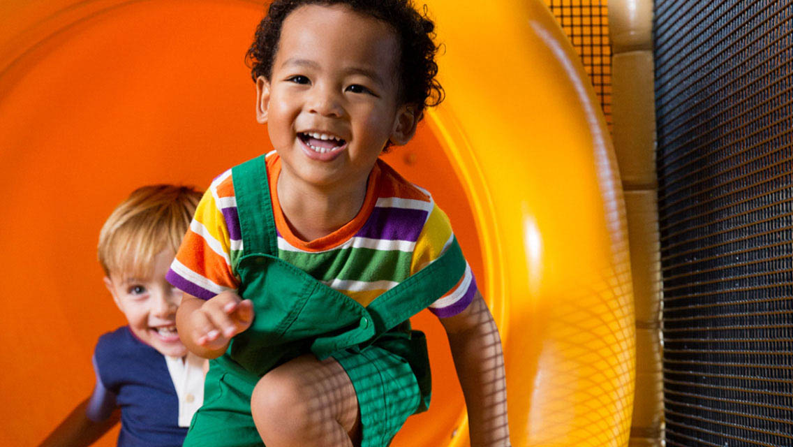 Two young children smile and laugh while playing on jungle gym equipment.