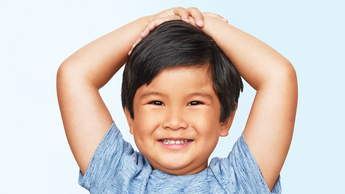 Young boy grinning with arms on his head