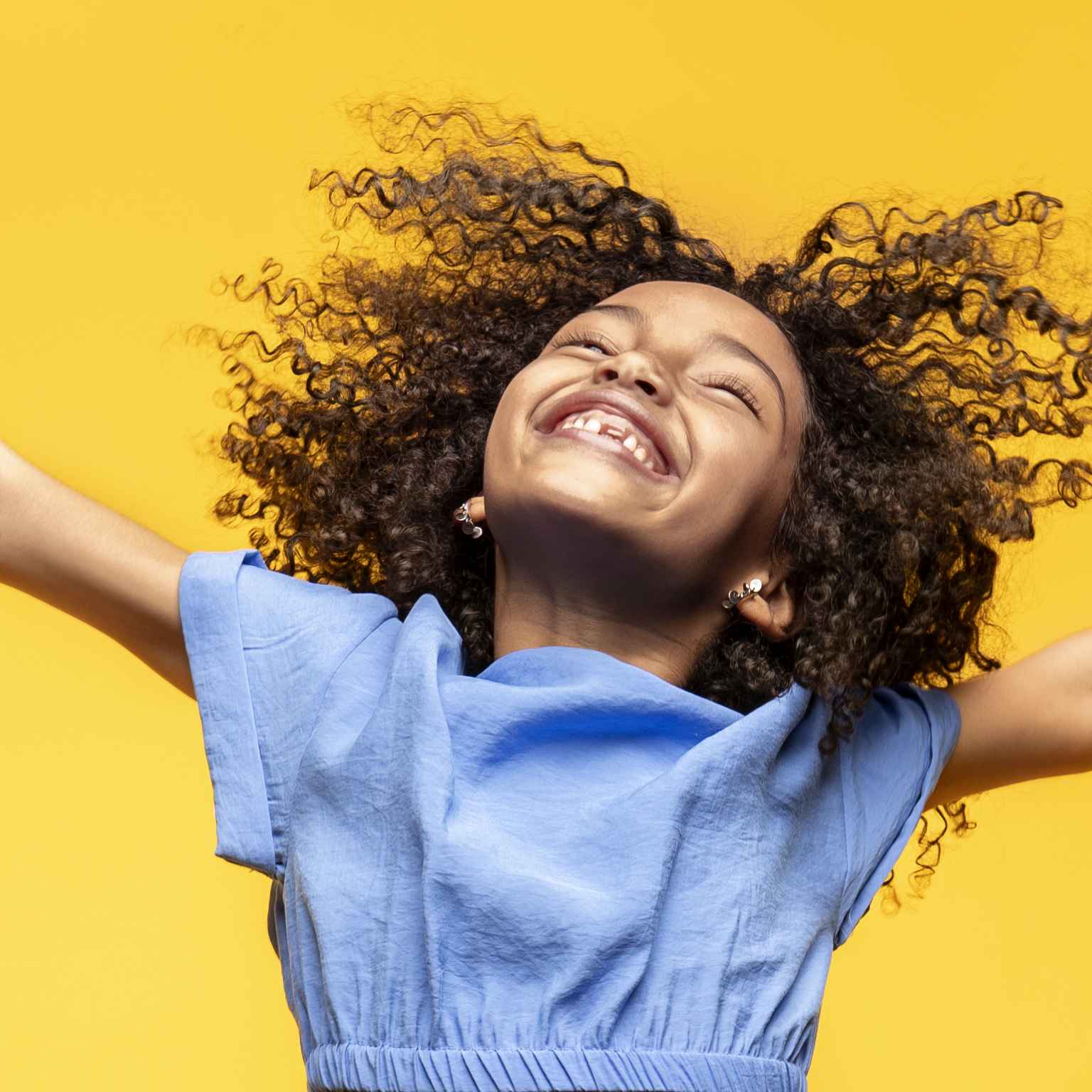 A child jumps for joy with outstretched arms and a happy smile