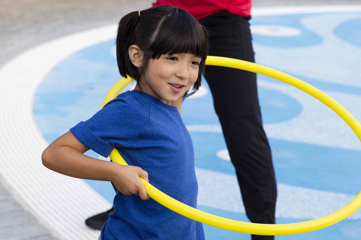 a girl in a blue shirt playing with a yellow hula hoop