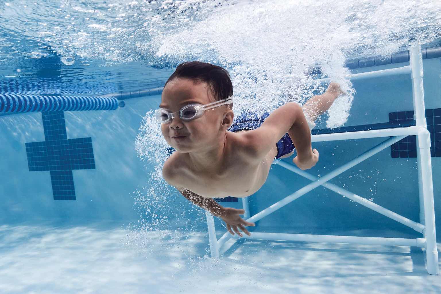 Young boy wearing goggles holding his breath and swimming underwater