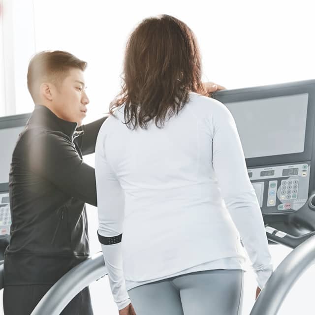 A trainer consults with his client, who is standing on a treadmill