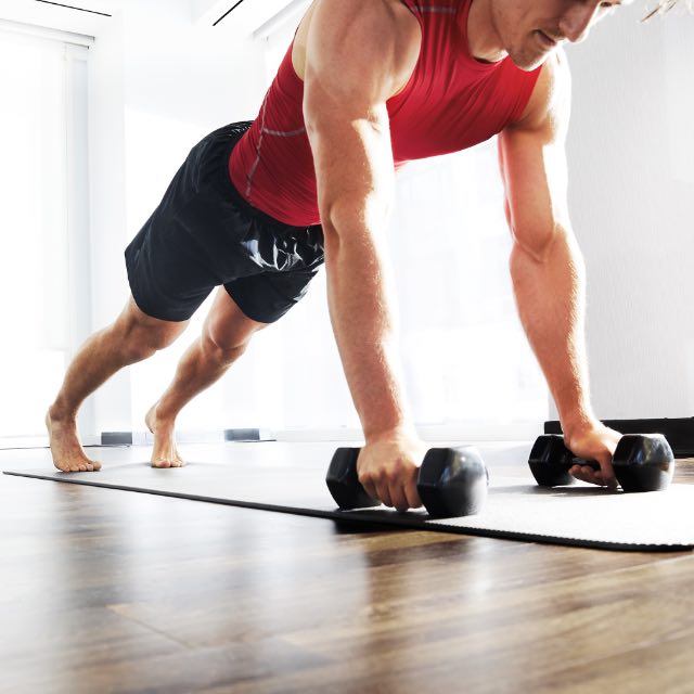 Two people in push up position with dumbbells. 