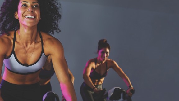 Two women participating in an indoor cycle class at Life Time