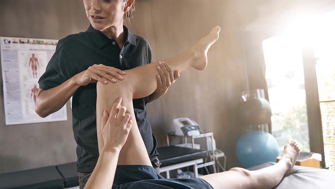 A physical therapist holding the leg of a client who is laying on their back on an adjustment table