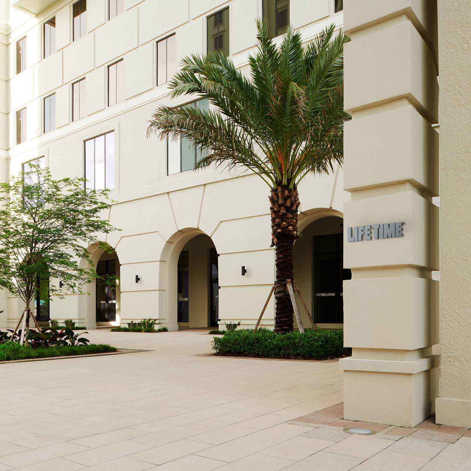 A line of trees stands in front of the sleek, beige exterior of Life Time Coral Gables 