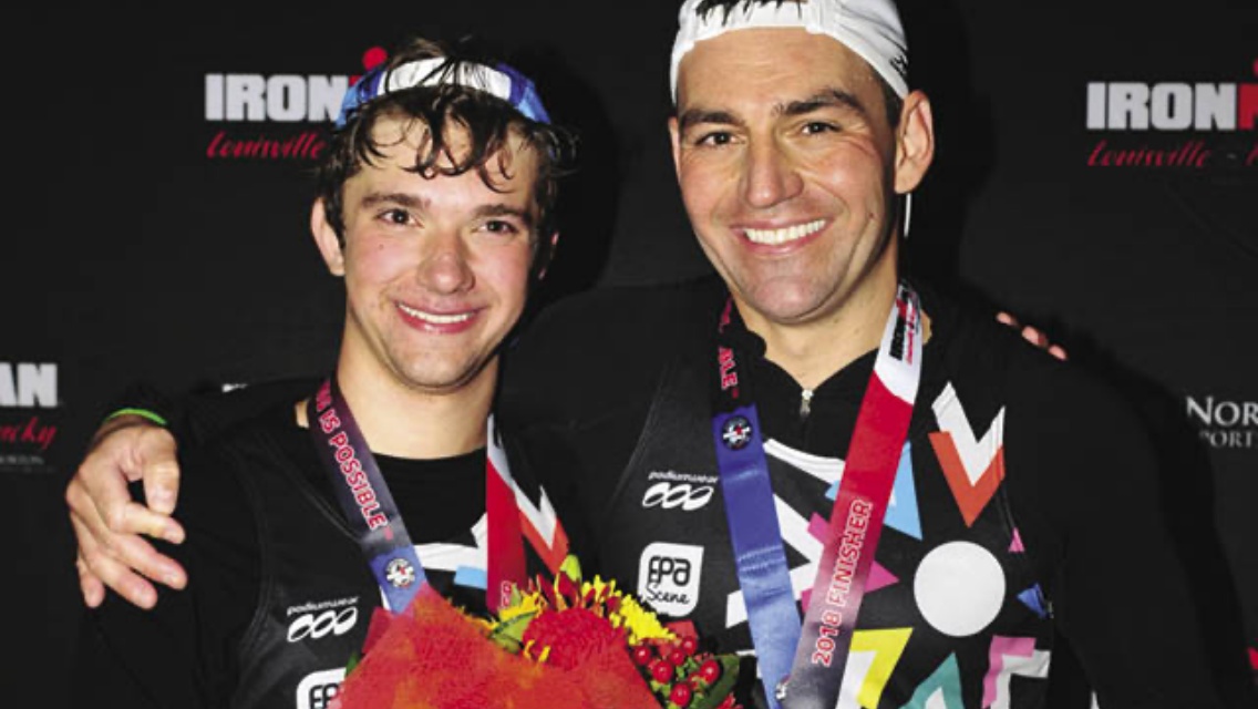 Two men with medals around their neck smiling at camera. 