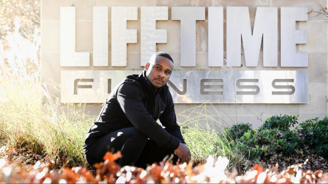 Image of man in front of Life Time Fitness sign. 
