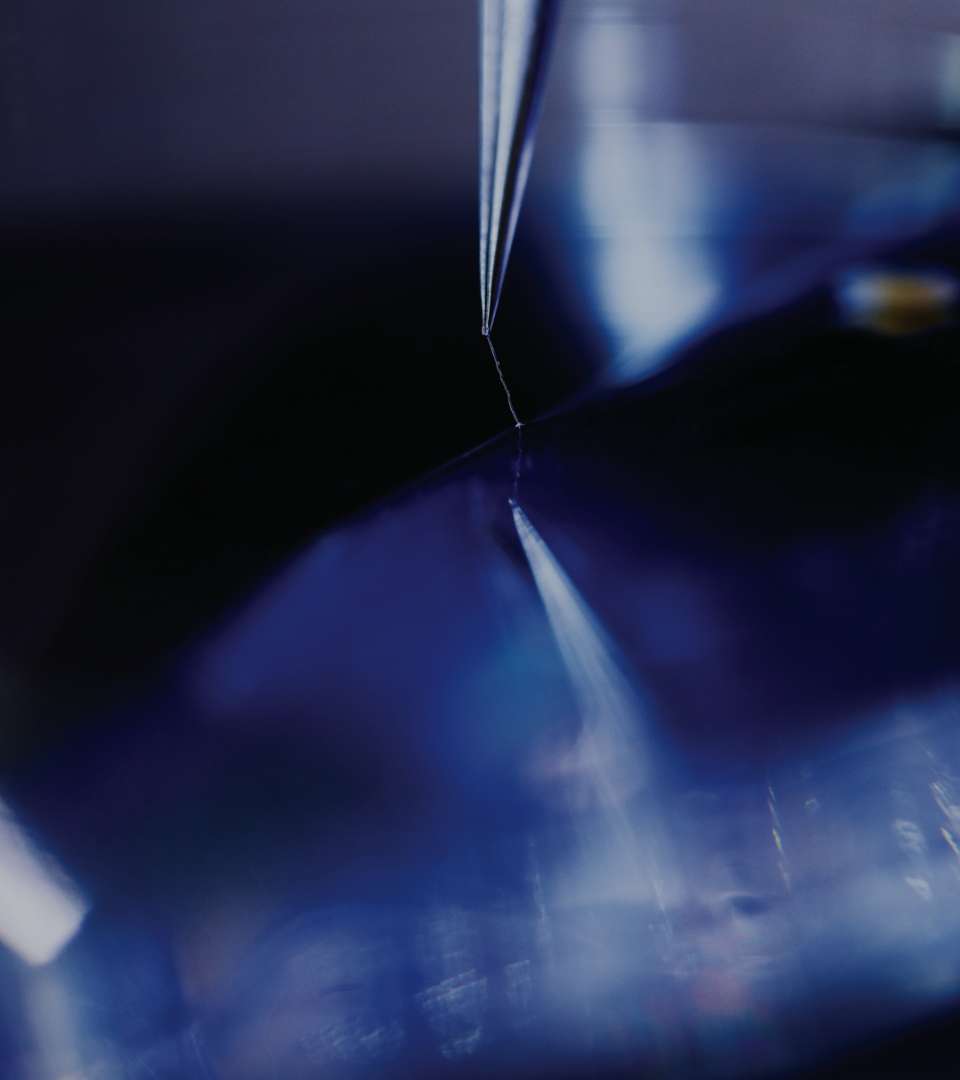 a close up, abstract image of the end of a needle touching a blue, reflective surface